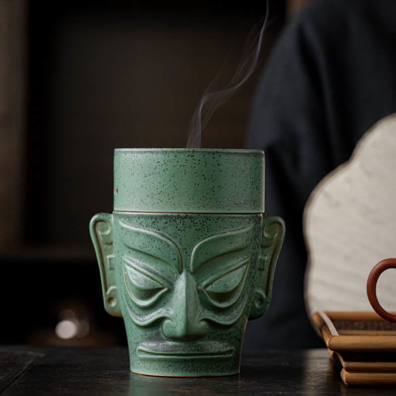 Sanxingdui Bronze Mask Incense Burner – Frontal view with smoke, wooden tray and tea ware in soft focus