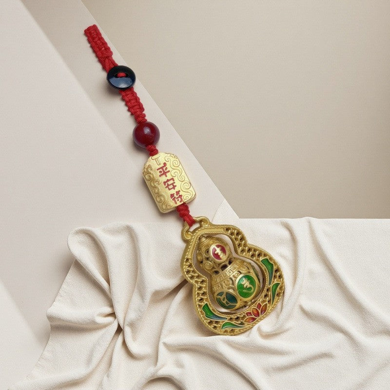 Gold filigree calabash keychain with peace talisman and red cord draped on white fabric