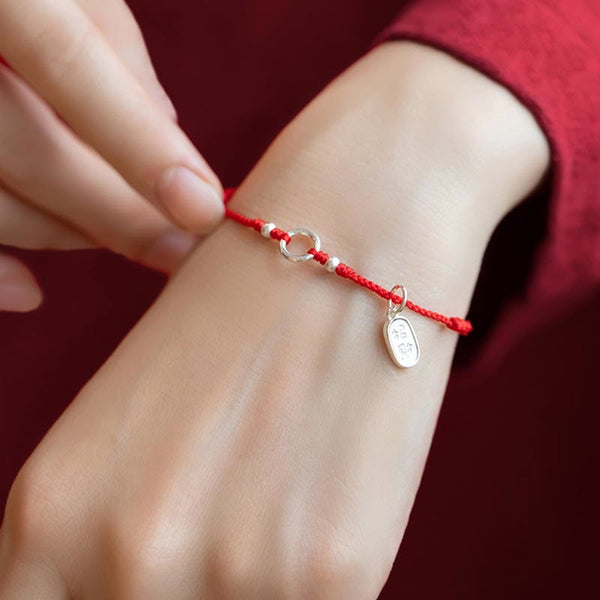Sterling Silver Lotus Peace Buckle Red String Bracelet – Wrist shot showing the bracelet worn with silver ring, beads, and leaf charm on braided red cord over a red sleeve