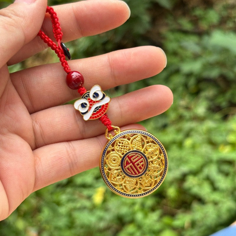 Hand holding gold rotating calabash disc keychain with lion dance charm and red cord, outdoor