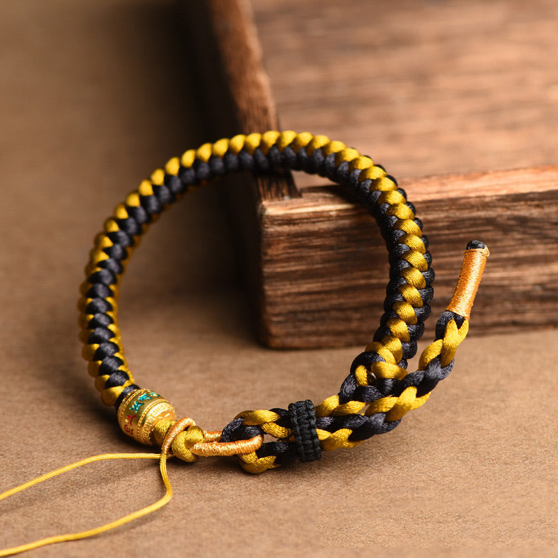 Tibetan Black Gold Dragon Scale Bracelet – angled on rustic wood blocks, black and gold braided cord, adjustable knot