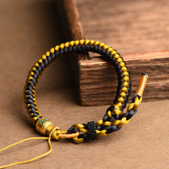 Tibetan Black Gold Dragon Scale Bracelet – angled on rustic wood blocks, black and gold braided cord, adjustable knot