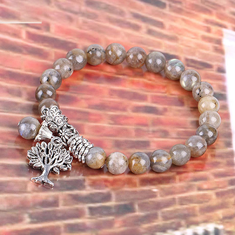Tree of Life labradorite bracelet with gray beads and blue-green labradorescence, silver tree of life charm, brick patterned background.