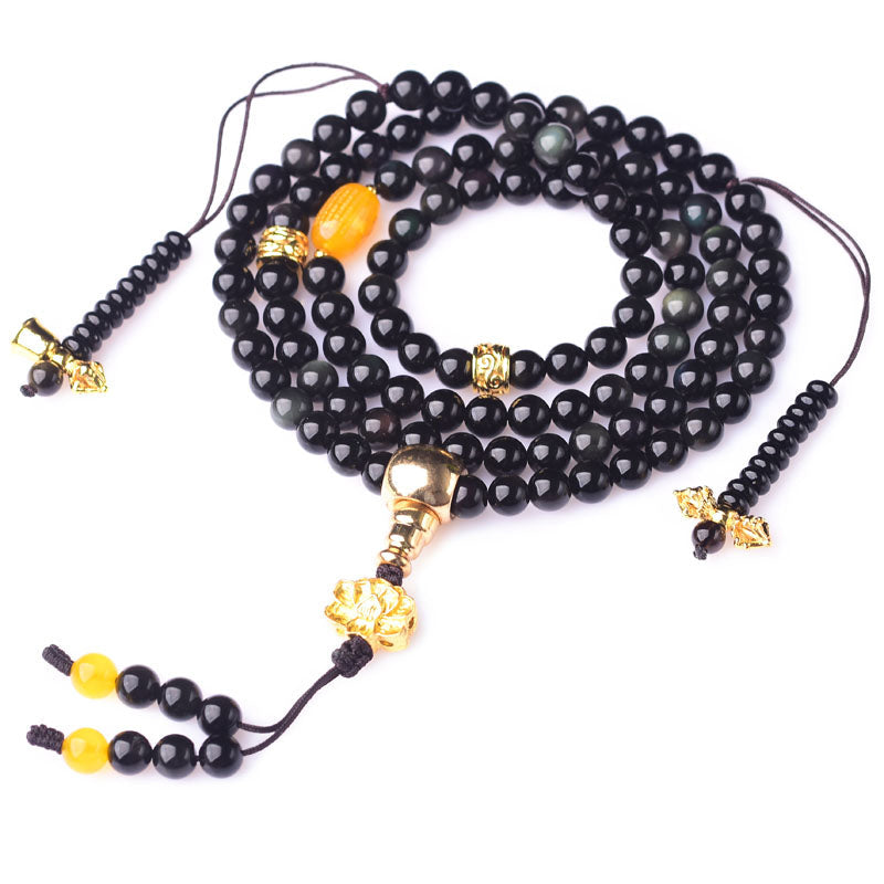 Black Obsidian Lotus Mala Bracelet - Coiled spiral on white background, gold lotus tassel visible, obsidian