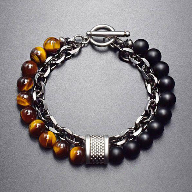 Tiger Eye Lazurite Malachite Protection Bracelet – Top-down view of men's bracelet with tiger's eye and black onyx beads, silver curb chain, textured barrel spacer, and toggle clasp on gray surface