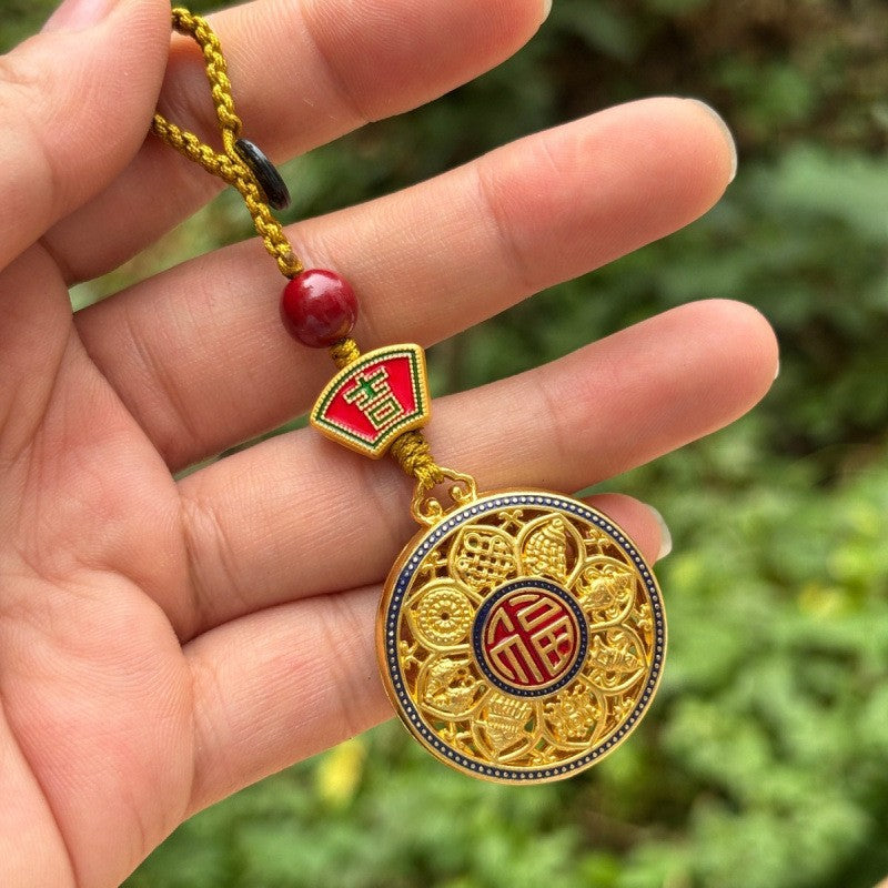 Hand holding gold rotating calabash disc keychain with longevity symbol and red bead, outdoor