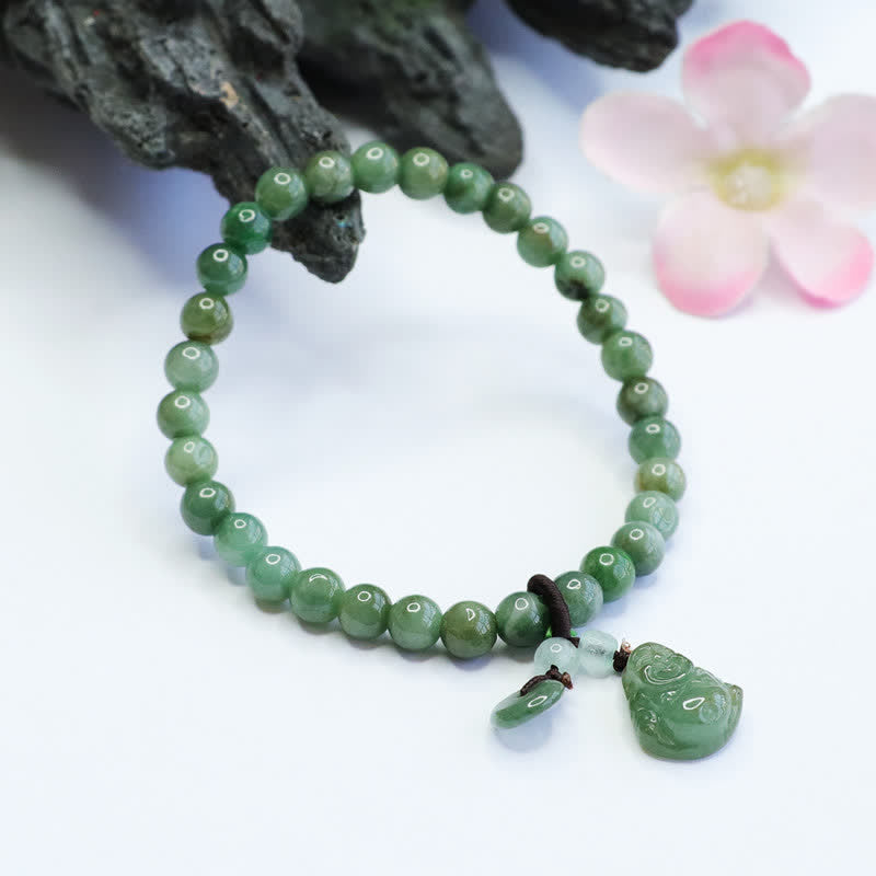 Cyan jade beaded stretch bracelet with carved Laughing Buddha figure and jade disc charm, white background with driftwood and pink flower prop accents