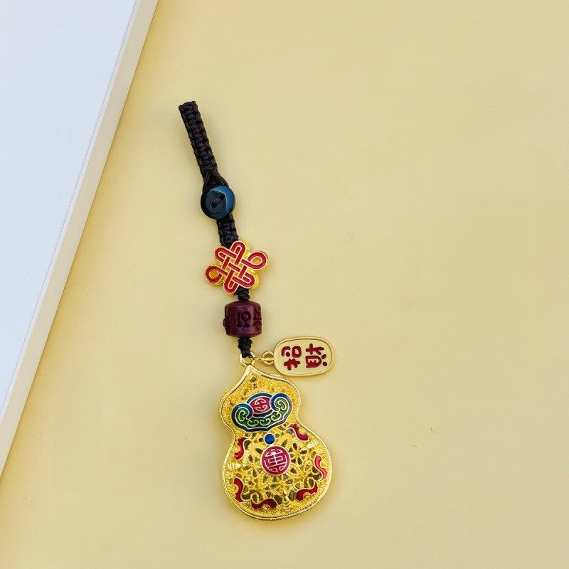Gold filigree calabash keychain with peace talisman, red agate and gold cord on ceramic vase