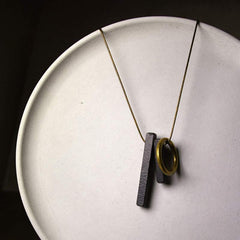 Zen Circle Ebony Wood Necklace - black bar and gold ring pendant on white ceramic plate, artisan flat lay