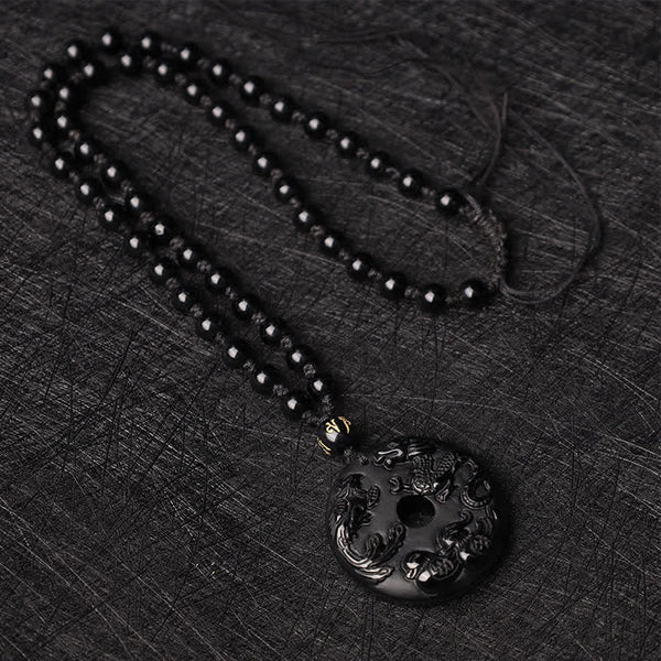 Black Obsidian Dragon Phoenix Pendant - Flat-lay beaded necklace with carved obsidian disc on dark textured fabric, Luck
