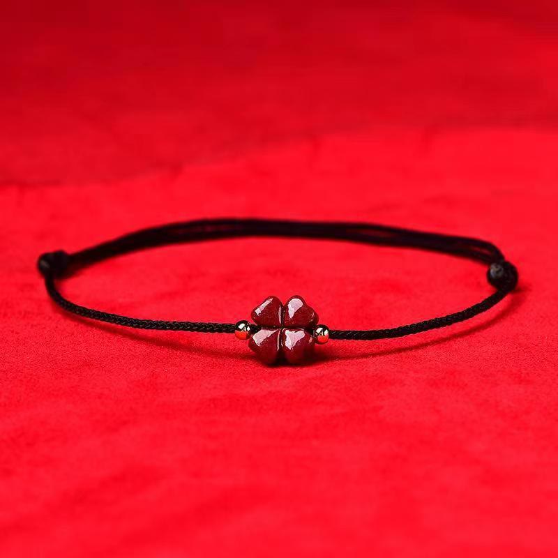 Black cord adjustable bracelet with cinnabar four leaf clover carved vermilion charm gold spacer beads and sliding knot closure on red velvet fabric background