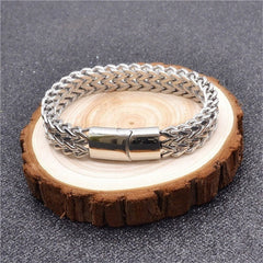 Fish Scale Titanium Steel Magnetic Bracelet – silver braided chain on natural wood slice stand, gray textured surface, elevated shot