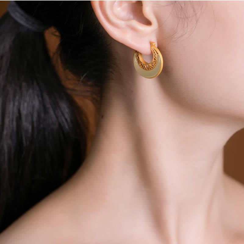 Crescent Moon Jade Drop Earrings – Gold hoop earrings with white jade crescent and geometric lattice on layered teal velvet and tan fabric, side angle shallow depth