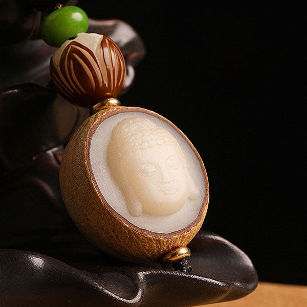 Bodhi Seed Blessing Keychain - macro detail of Buddha head carving emerging from split seed shell on dark stand, enlightenment