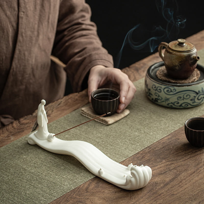 Buddha Monk Sea Wave Mountain Ceramic Incense Burner – White ceramic monk on waves with smoke rising beside tea cup, meditation space
