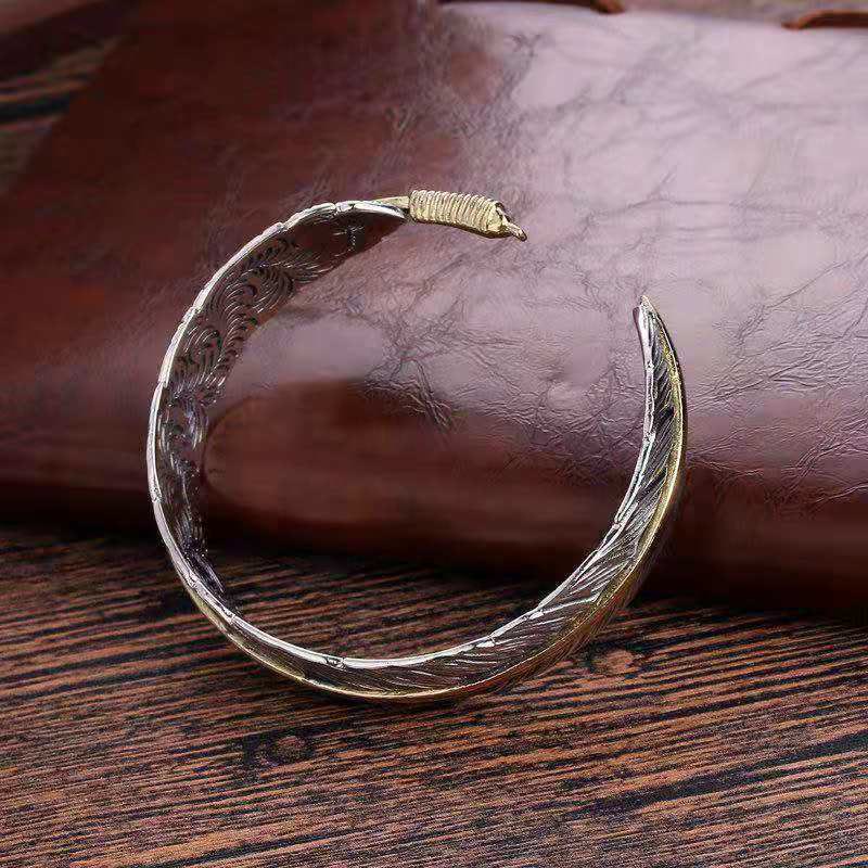 Antique silver feather cuff bracelet with gold wire-wrapped terminal, oxidized finish and engraved barb texture on leather and wood surface