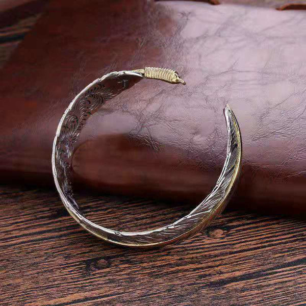 Antique silver feather cuff bracelet with gold wire-wrapped terminal, oxidized finish and engraved barb texture on leather and wood surface