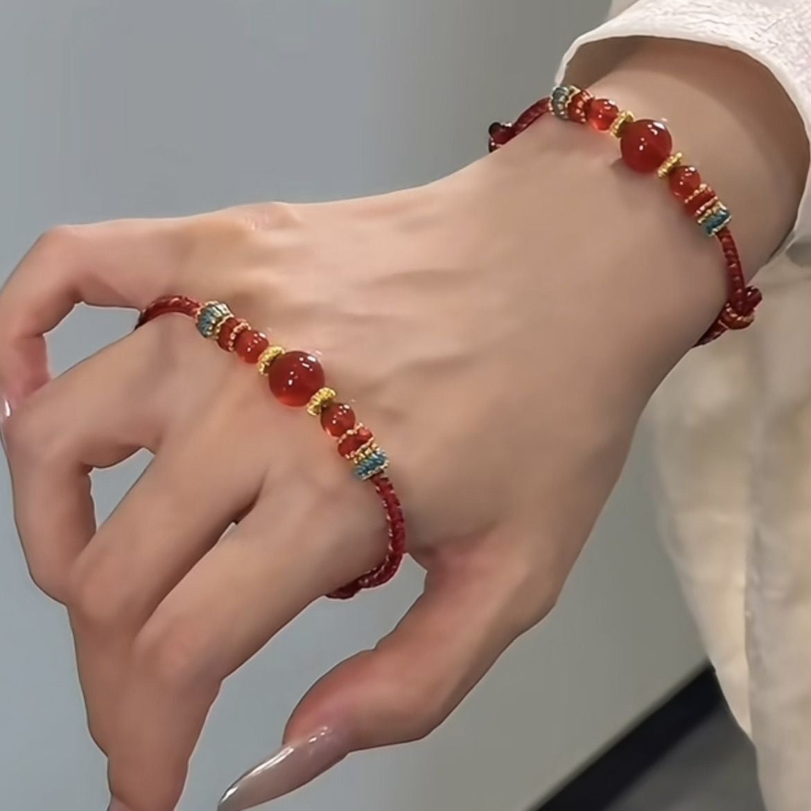 Dunhuang Agate Bracelet – red braided bracelet worn on back of hand with white lace sleeve visible, elegant crystal wristwear