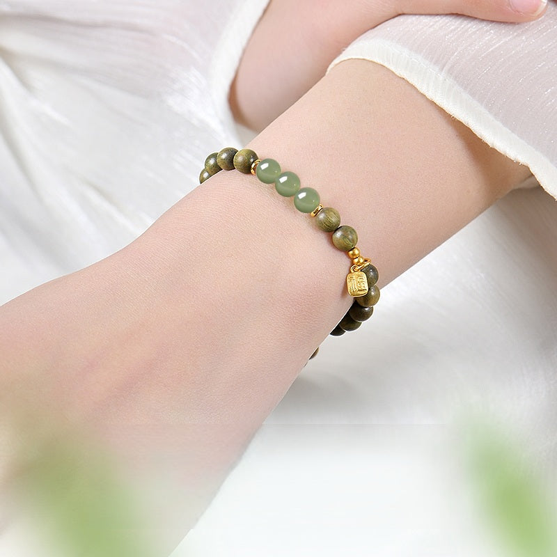 Green Sandalwood Bracelet – Worn on wrist with green jade beads and gold charm, white sleeve, natural wood