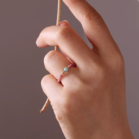 Gemstone Bead Ring – hand wearing pink beaded ring with turquoise stone, holding gold chain, gray background, natural gemstone