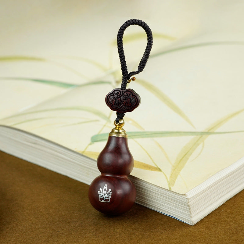 Red sandalwood gourd keychain with guardian symbol resting on open book