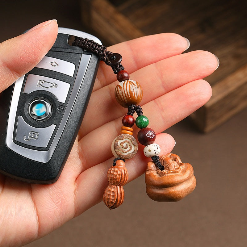 Hand holding car keys with peach wood Feng Shui keychain featuring peanut and persimmon