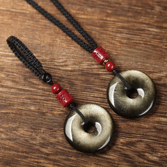 Gold Obsidian Pendant – Two gold sheen obsidian peace buttons with black cord and red beads on wood, grounding jewelry