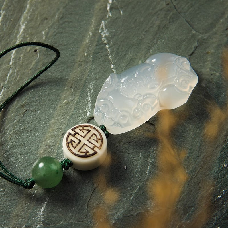 Chalcedony Pixiu Keychain – close-up of carved pixiu on gray stone slab with symbol bead