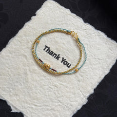 Double-Layer Gourd Bracelet – Gold chain and blue braided rope with gourd charm on white felt, feng shui protection