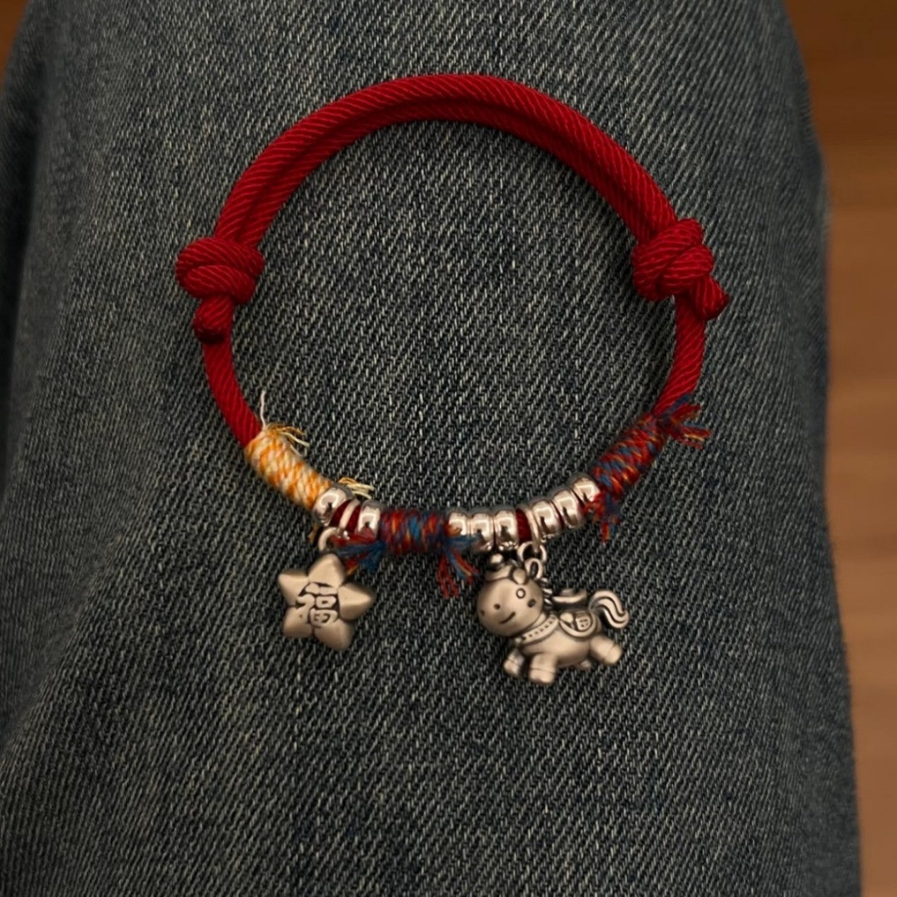 Horse Red String Bracelet – Red string bracelet with silver horse charm lying on dark denim fabric, couple