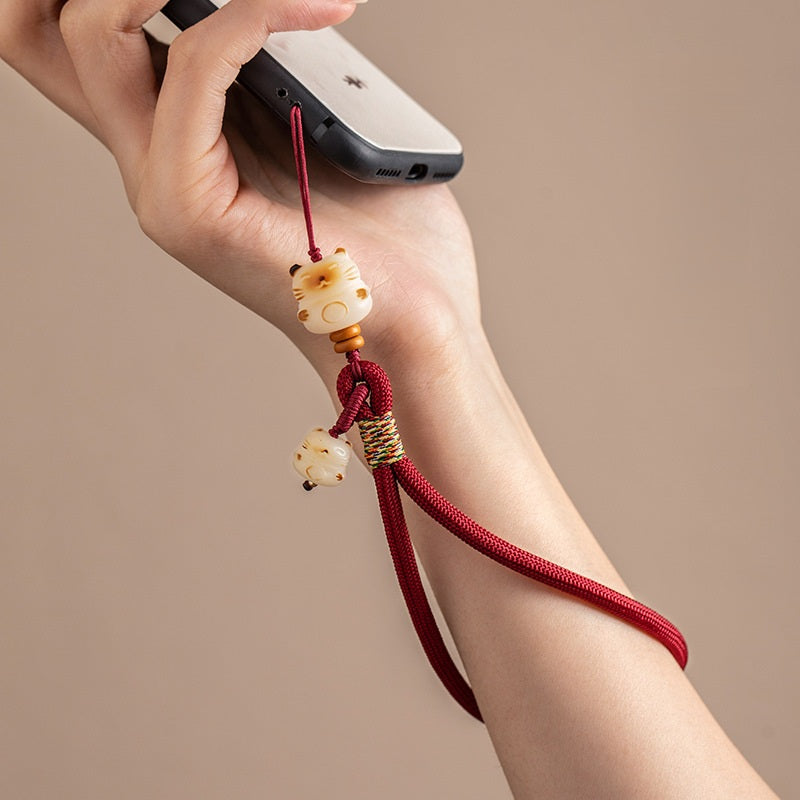 Model holding a smartphone with wine red Bodhi Maneki Neko wristlet strap on wrist