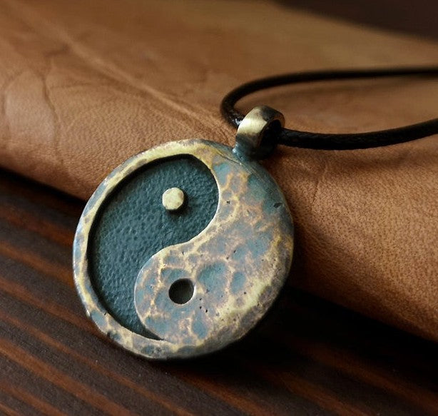 Yin Yang Pendant – patina bronze pendant resting on hand over dark wood, blue-green oxidation tones