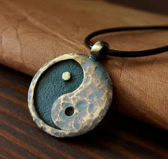 Yin Yang Pendant – patina bronze pendant resting on hand over dark wood, blue-green oxidation tones