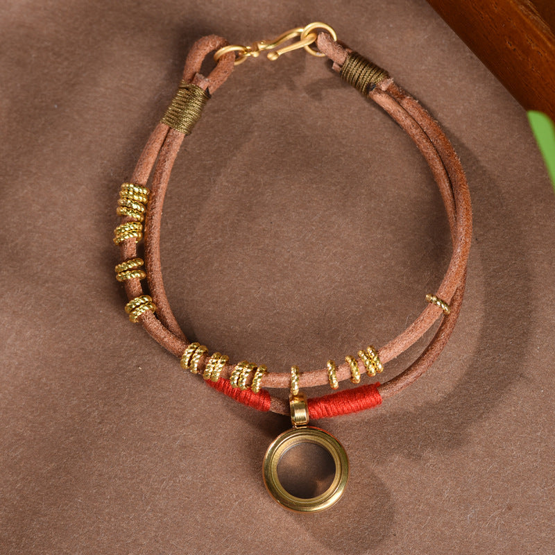 Gau Box Bracelet – top view brown leather band with gold clasp and locket on brown surface, spiritual accessory