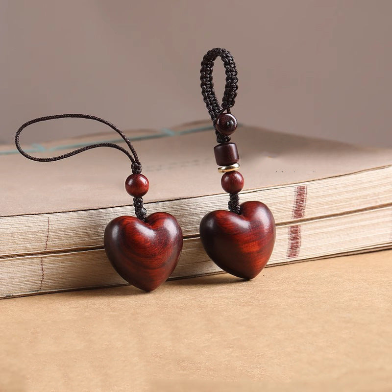 Rosewood Heart Keychain – two heart pendants side by side, silk and braided cords on stacked books
