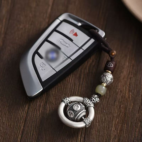 Mantra Keychain – silver prayer wheel charm hanging from BMW car key, dark wood surface