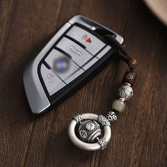 Mantra Keychain – silver prayer wheel charm hanging from BMW car key, dark wood surface