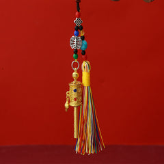 Tibetan Prayer Wheel Keychain – gold-tone prayer wheel pendant with colorful silk tassel, turquoise beads and auspicious knot charm, red background, front vertical view