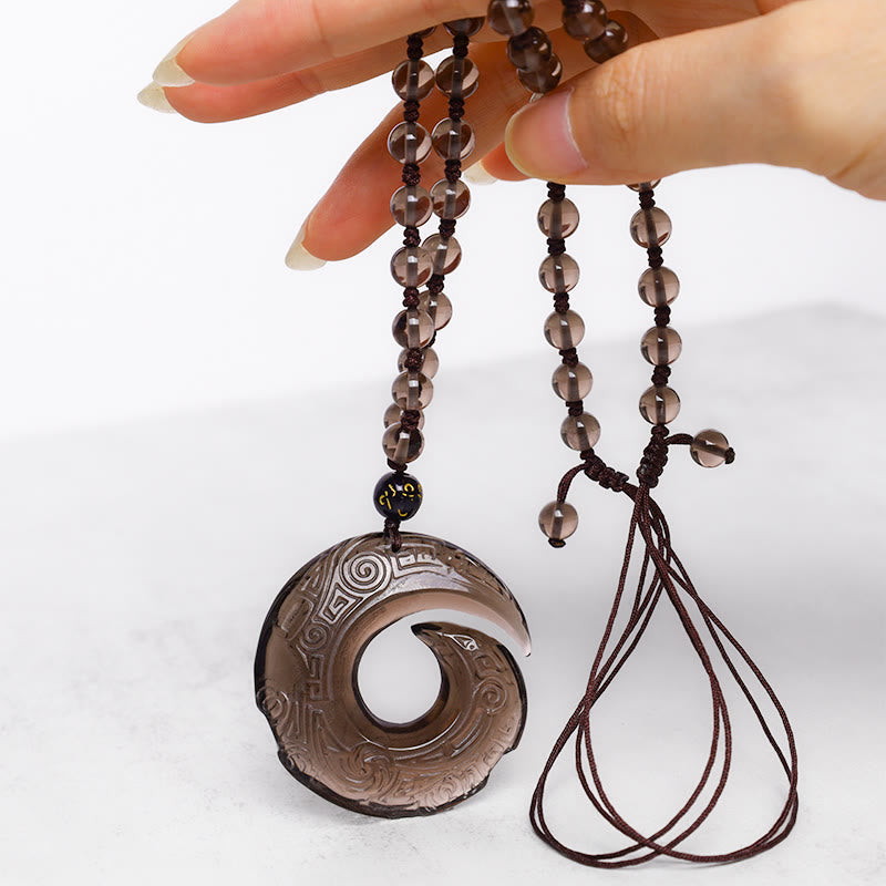 Black Obsidian Ice Obsidian Pendant Necklace – Hand-held smoky quartz spiral pendant showing translucent brown stone with intricate carved patterns, gold Sanskrit accent bead, adjustable macrame cord closure, white studio photography, natural crystal healing necklace
