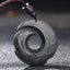 Hetian Cyan Jade Peace Buckle Luck Necklace – Dark green carved jade pendant with spiral cutout design, traditional cloud motifs, and black braided cord on dark background