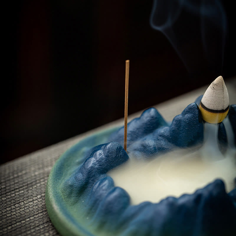 Ceramic Backflow Incense Burner – Glazed blue mountain with smoke waterfall and rising wisps on gray mat, meditation