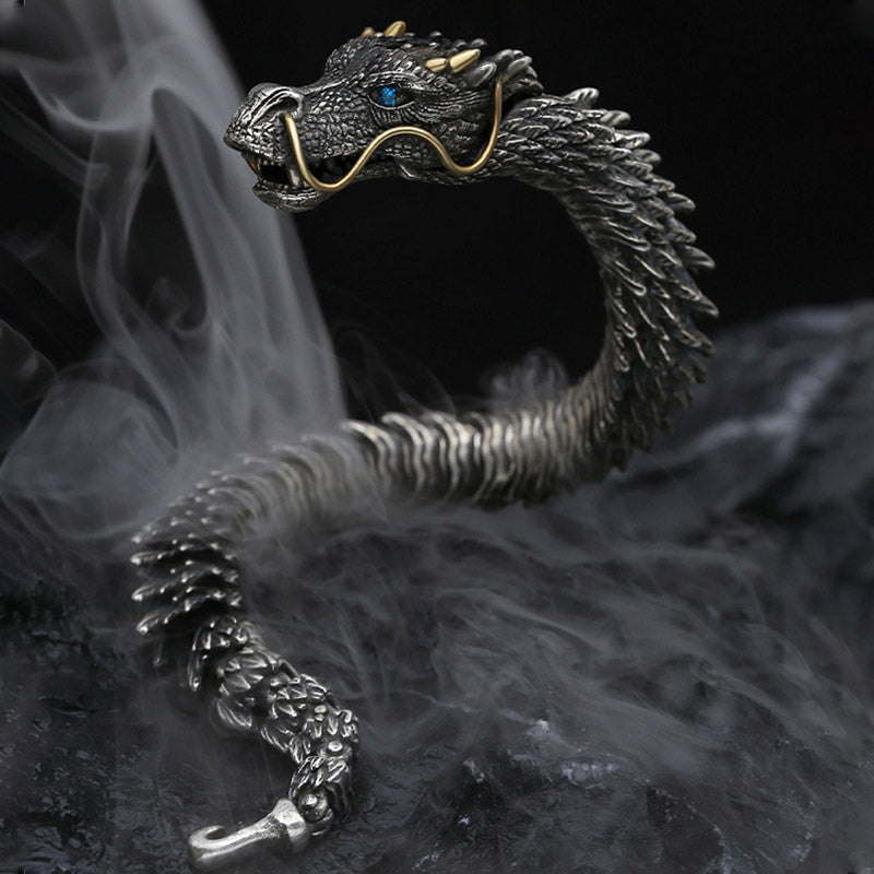 Eastern dragon themed cuff bracelet with oxidized silver scales gold horn accents blue sapphire eye and detailed facial features shown against smoky dark background