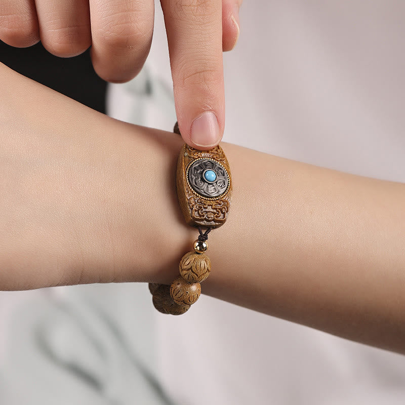 Green Sandalwood & Ebony Soothing Bracelet – wrist close-up of scroll-carved barrel charm with blue turquoise center, wood...