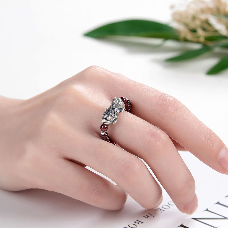 Silver Garnet PiXiu Ring – Ring worn on finger with green leaf and white flower backdrop
