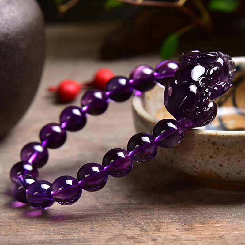 Amethyst PiXiu Fortune Bracelet – Side view purple beads on rustic wood with ceramic bowl, luck charm
