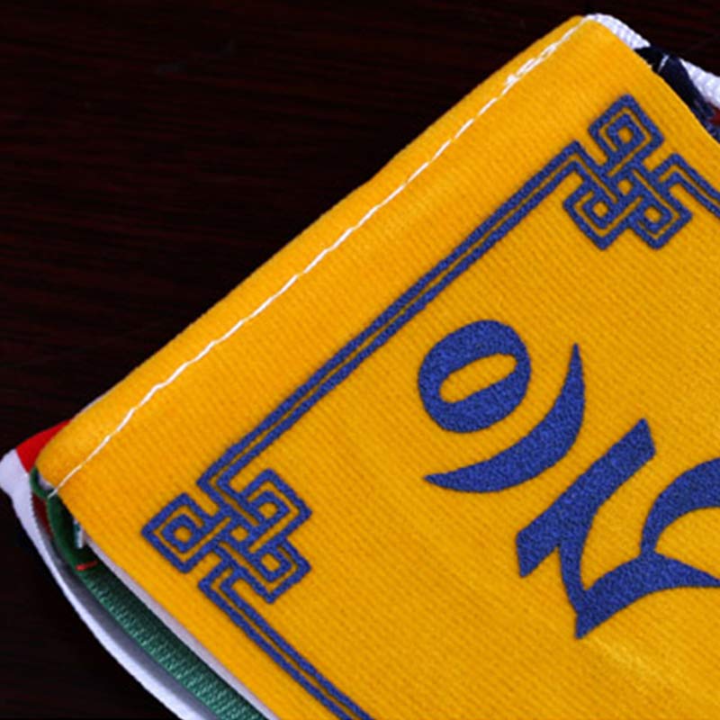 Tibetan Prayer Flags – Yellow flag with blue embroidered Tibetan script and endless knot, fabric close-up