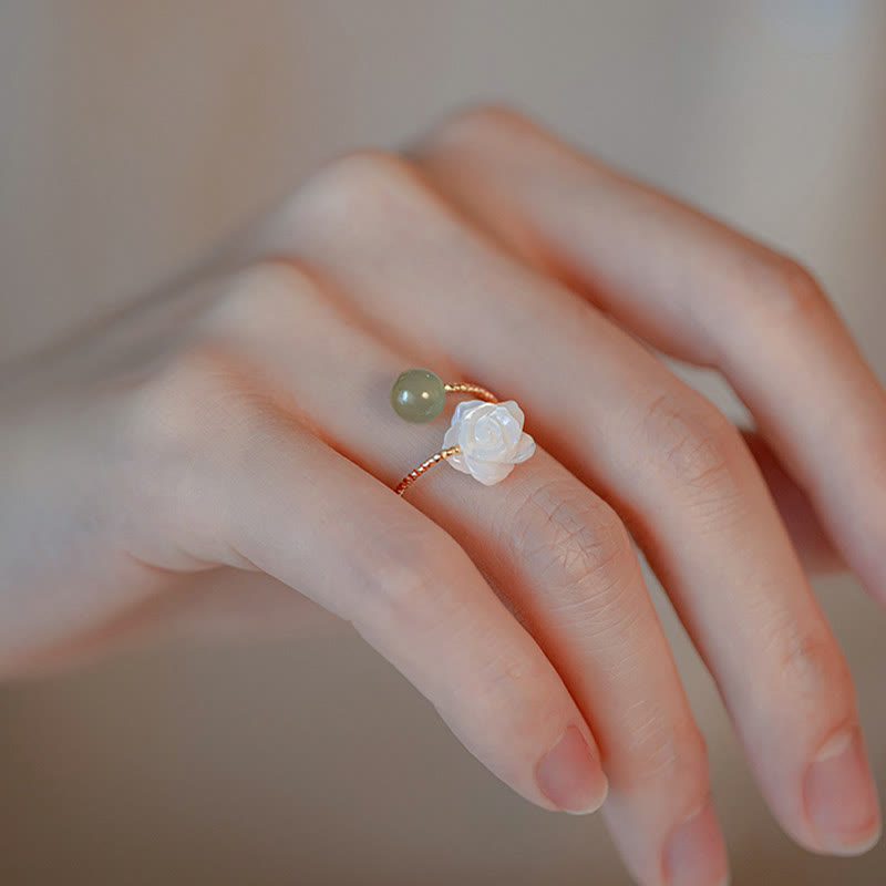 14K Gold Tridacna Jade Rose Ring – Rose gold open ring with white carved lotus and green jade bead on finger, warm beige bokeh lifestyle shot