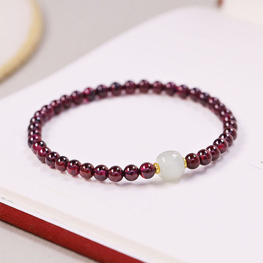 Garnet and jade beaded bracelet with translucent pale green nephrite jade centerpiece flanked by gold-toned spacers, elegant minimalist jewelry on white surface