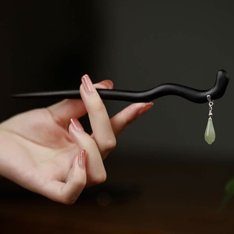 Hand displaying the full length of curved ebony wood hairpin with silver jade tassel