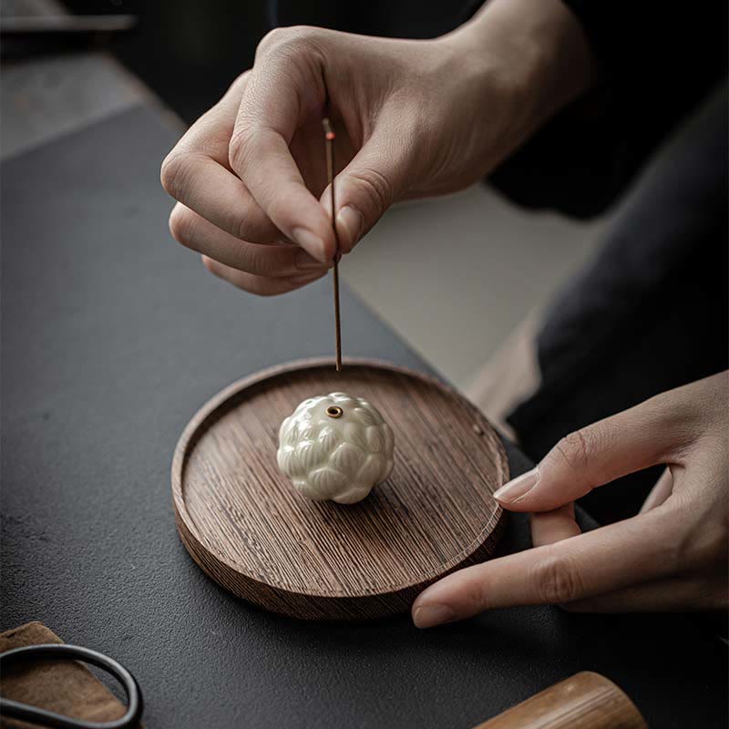 Ceramic Lotus Incense Burner with hand inserting incense stick on wooden tray, mindful